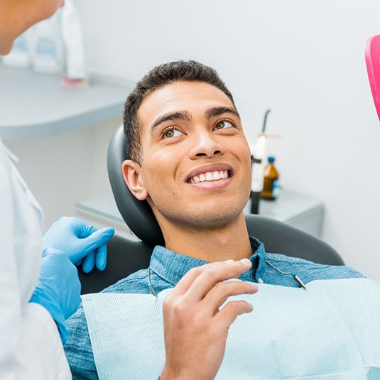 Patient smiling while holding small, pink mirror