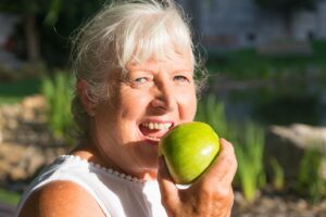 Older woman with dentures about to bite into apple.